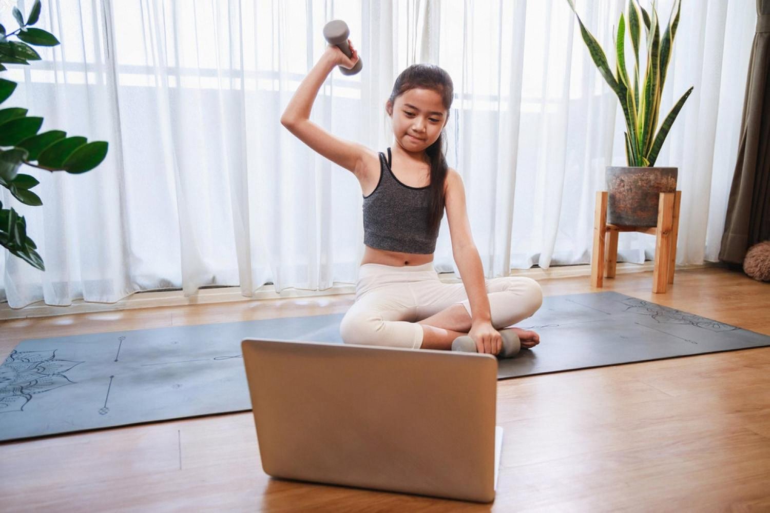 Young child practising a hands-on activity at home with a laptop and exercise mat